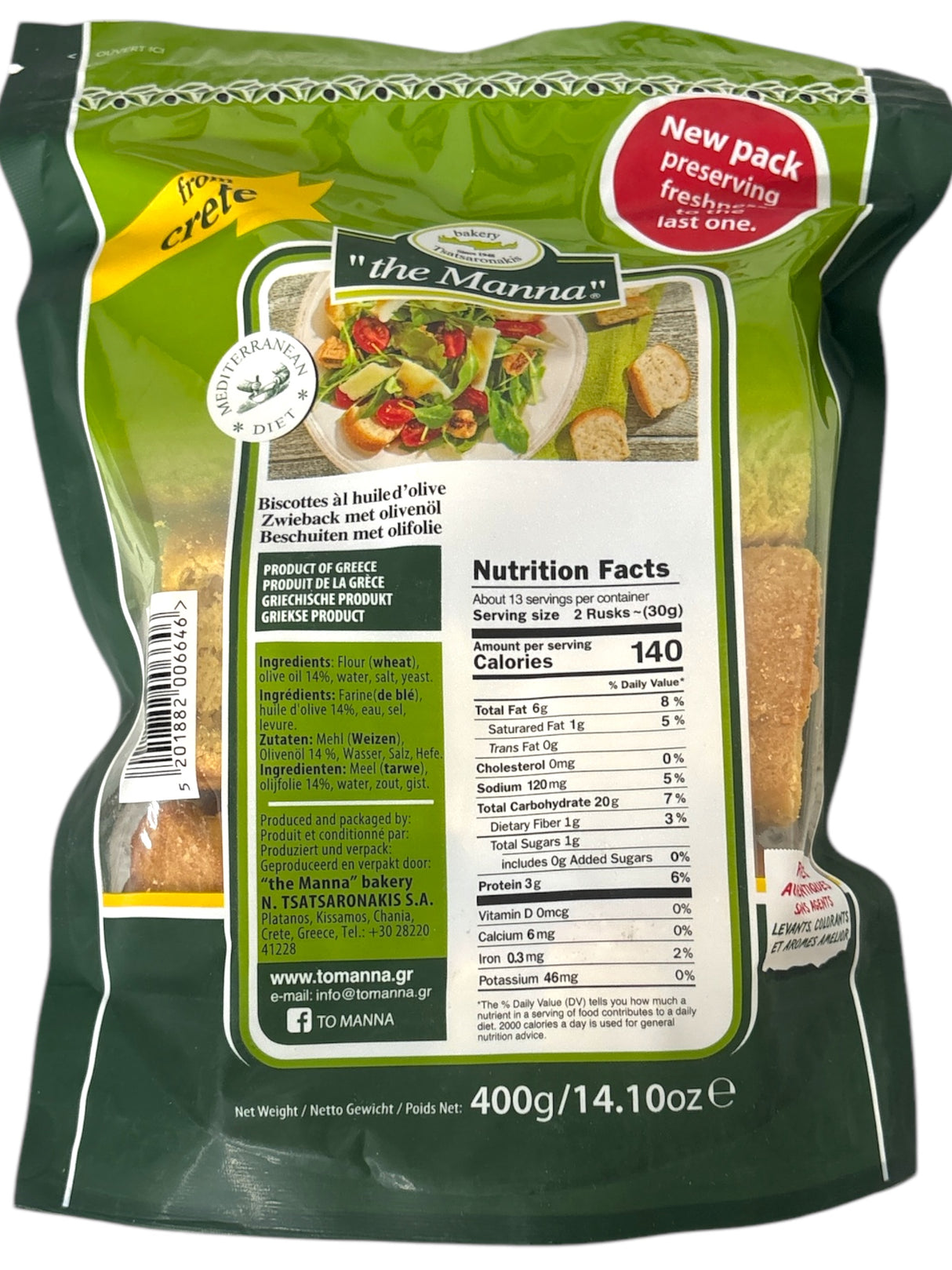 A package of "the Manna" rusks from Crete. The package has a green color theme with a photo of a salad bowl and slices of the rusks. A red label says “New pack preserving freshness.” Nutritional facts are displayed, showing that a serving (2 rusks, about 30g) has 140 calories. The product is made from wheat flour and contains olive oil (14%). The packaging highlights that the product is from Greece and has the website and contact info of "the Manna" bakery, located in Chania, Crete. The package weighs 400g