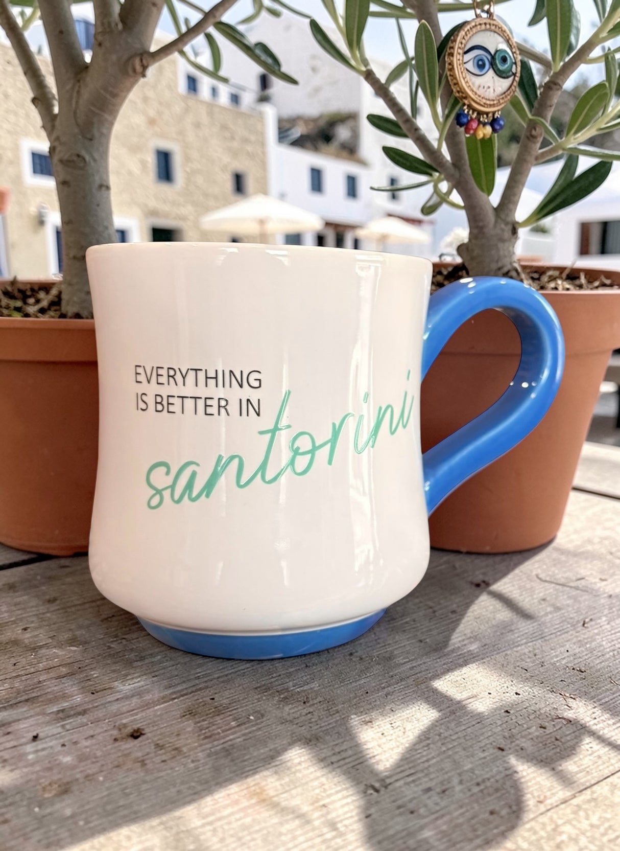 Mug with 'Everything is better in Santorini' text on a wooden surface with plants in the background