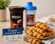 Greek Frappé Starter Kit with NESCAFÉ Classic coffee, shaker bottle with filter, and traditional Greek koulourakia cookies on a kitchen table.