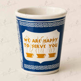 A white ceramic coffee mug with a blue Greek key border and a central white shield containing the text 'WE ARE HAPPY TO SERVE YOU' in orange, above three orange coffee cups. The mug is photographed on a light beige background with a faint repeating watermark.