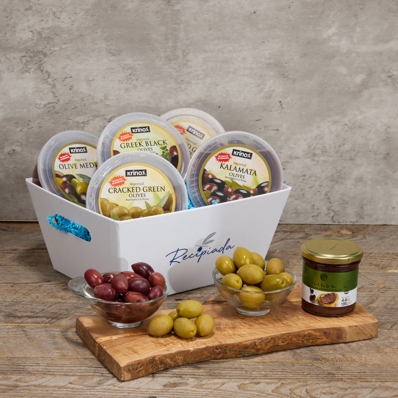 Assorted olive products including jars and bowls on a wooden surface with a concrete wall background.