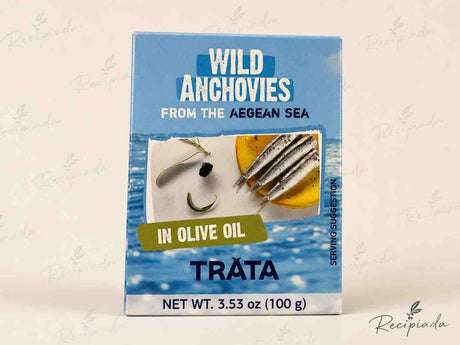 A box of Tráta Wild Anchovies from the Aegean Sea, in olive oil, shown on a light beige background with a faint watermark pattern.