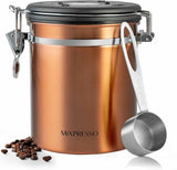A copper-colored stainless steel coffee bean canister with a black lid and silver clasp, shown with a metal measuring scoop and scattered coffee beans on a white background.