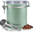 A mint green metal coffee bean canister with a clear lid and stainless steel clasp, shown with a metal measuring scoop and a small pile of coffee beans on a white background. The brand name 'Mixpresso' is printed on the front.
